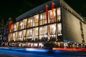 Außenansicht der Staatsoper Hamburg bei Nacht. Das Gebäude wir von außen mit blauen und roten Lichtern beleuchtet. Partner der NDR Kultur Karte.