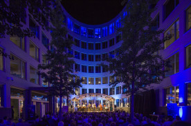 Fotografie der Eröffnung des Musikfestes Bremen. Die Bühne und die Zuschauerplätze sind in einem Innenhof aufgebaut. Das Foto wurde aus Sicht des Publikums Richtung Bühne geschossen.
