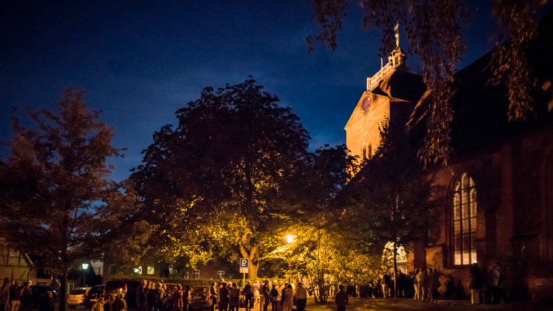 Foto bei Nacht Menschen stehen vor einer Kirche.