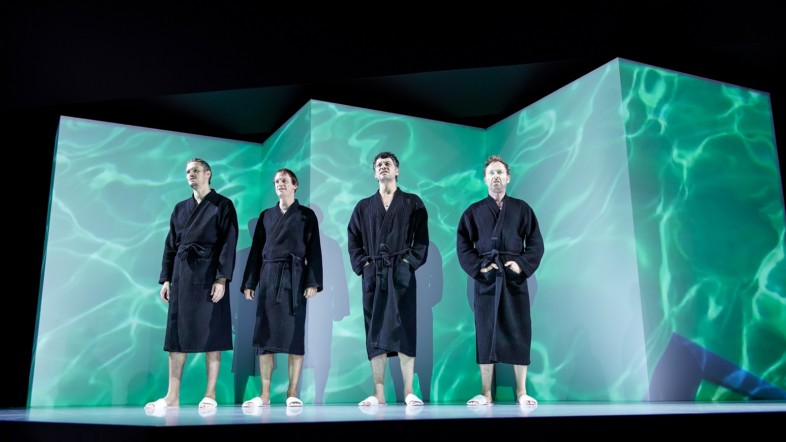 Vier Männer in schwarzer Kleidung stehen nebeneinander auf der Bühne vor einem grünen Hintergrund.