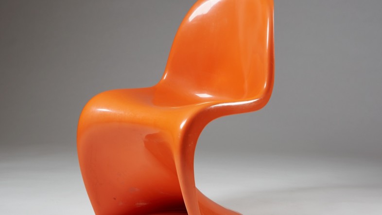 Fotografie eines Stuhls, der auf dem Boden vor einer grauen Leinwand steht. Der Stuhl ist orange.