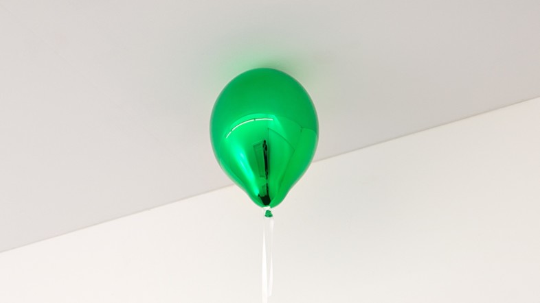 Foto eines grünen Ballons, der an der Decke eines hellen Raumes schwebt.
