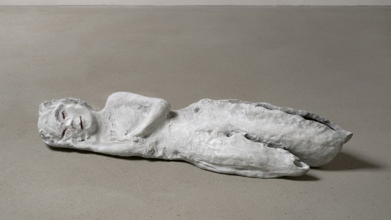 Foto einer Statue, die seitlich in schlafender Position auf dem Boden liegt.