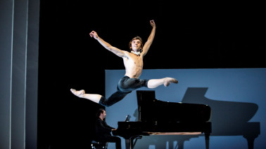 Ein Tänzer springt vor einem Klavier elegant durch die Luft.