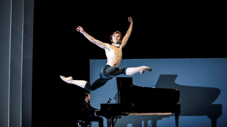 Ein Tänzer springt vor einem Klavier elegant durch die Luft.