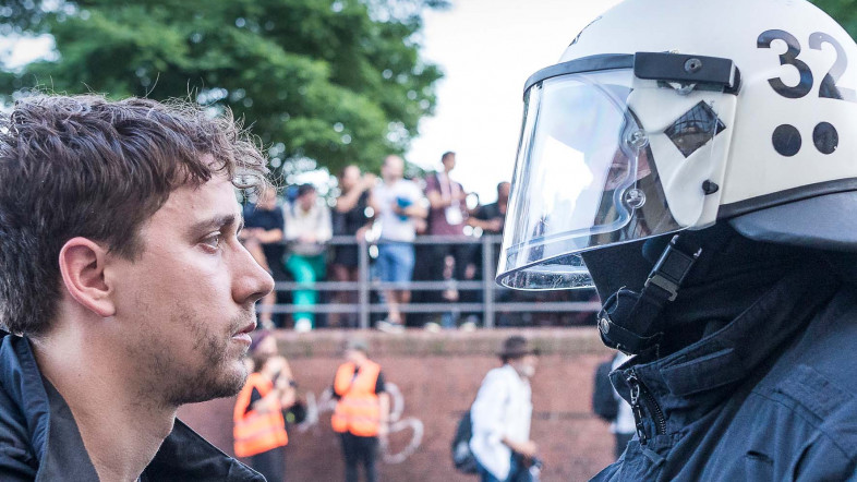 Ein Demonstrant steht einem Polizisten in Schutzmontur gegenüber.